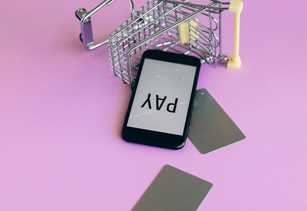 Shopping cart on its side with credit cards and smartphone fallen out to signify credit card debt that's gotten out of control